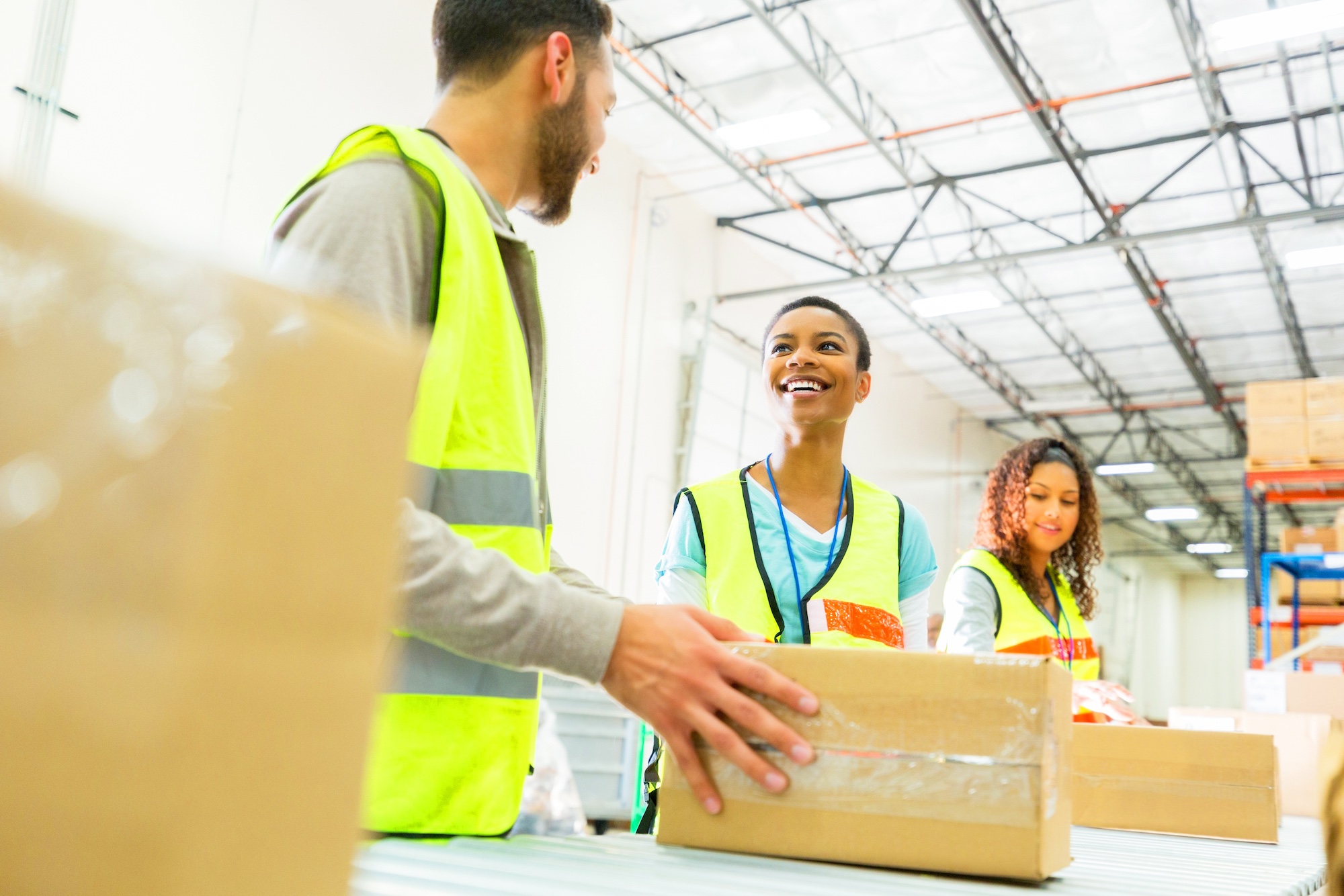 Three warehouse workers talking and laughing with boxes