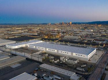 Aerial view of Prologis Vernon Business Center with Prologis globe logo on corner of building, located in Los Angeles, California with LA in city skyline in the distance.