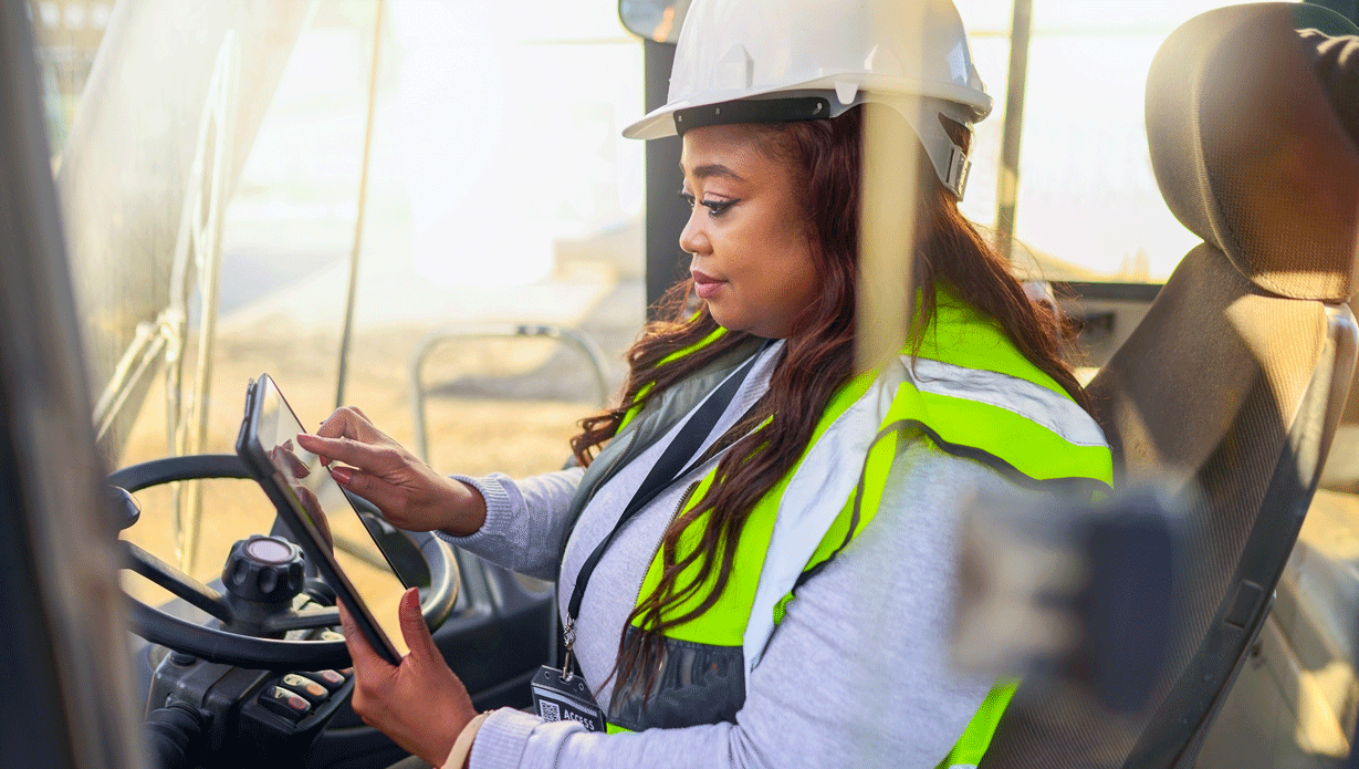 Woman driving a forklift in a white hard hat and safety vest