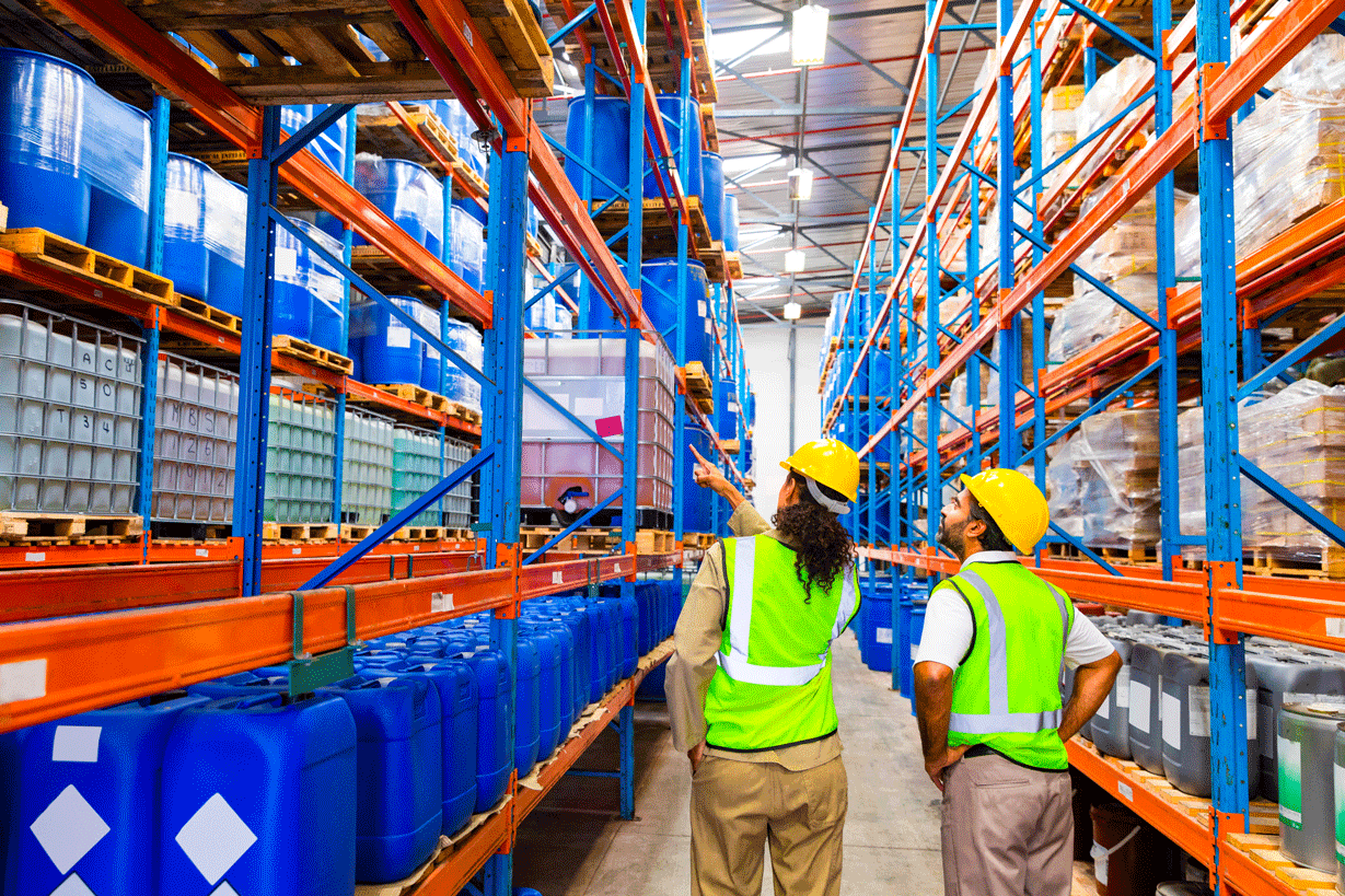 Two people walking in a warehouse in safety vests and hard hats