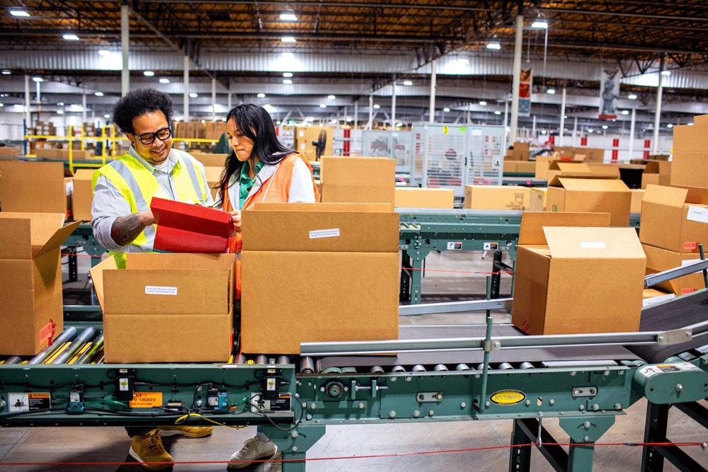 Two warehouse workers next to a conveyor system.